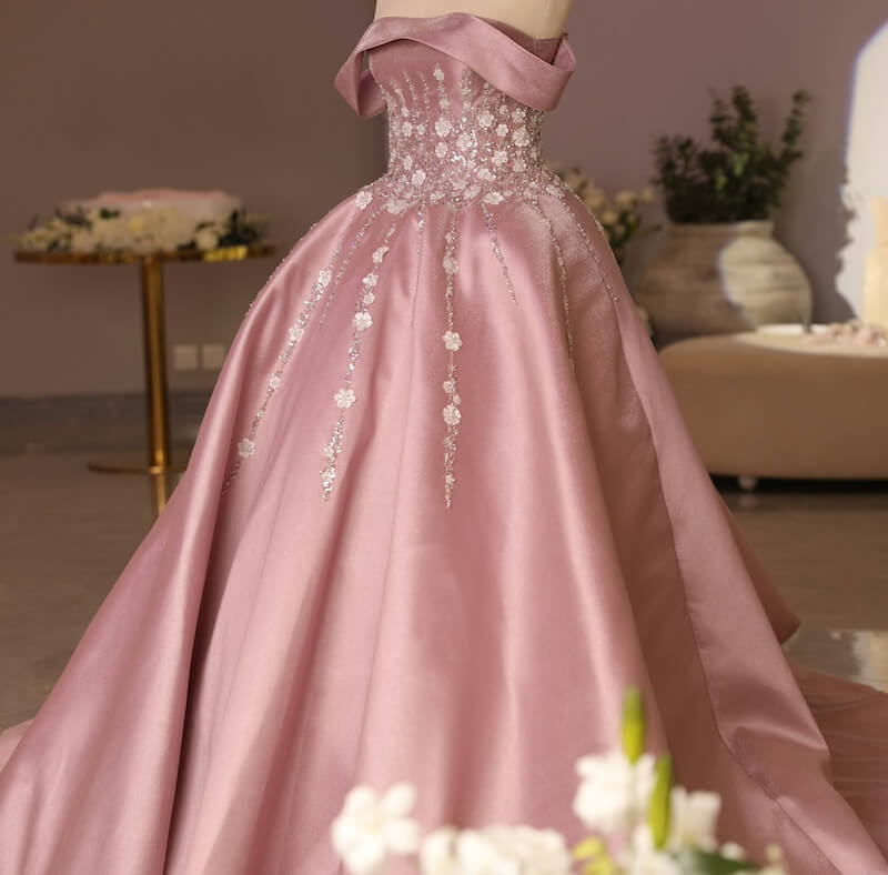 A pink ball gown with floral lace embellishments on the bodice and skirt, displayed in an elegant room.