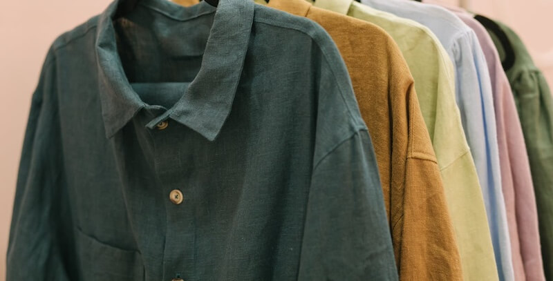 A row of button-up shirts in various colors, including teal, brown, green, and purple, hanging on a rack.