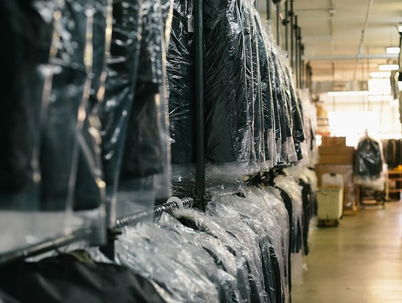 Rows of hanging garments covered in plastic bags in a warehouse setting.