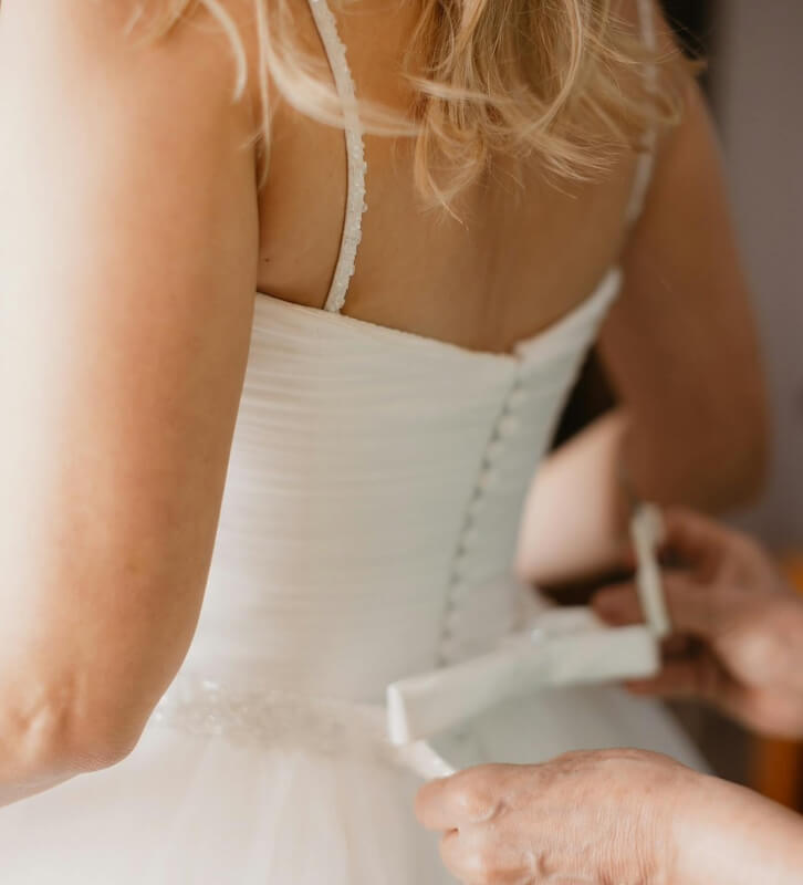 wedding dress alterations A person in a white wedding dress is being assisted with adjustments at the back.