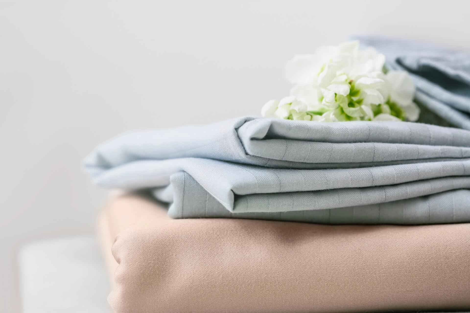 Folded beige and light blue fabric stacked on a surface with a small bunch of white flowers placed on top.